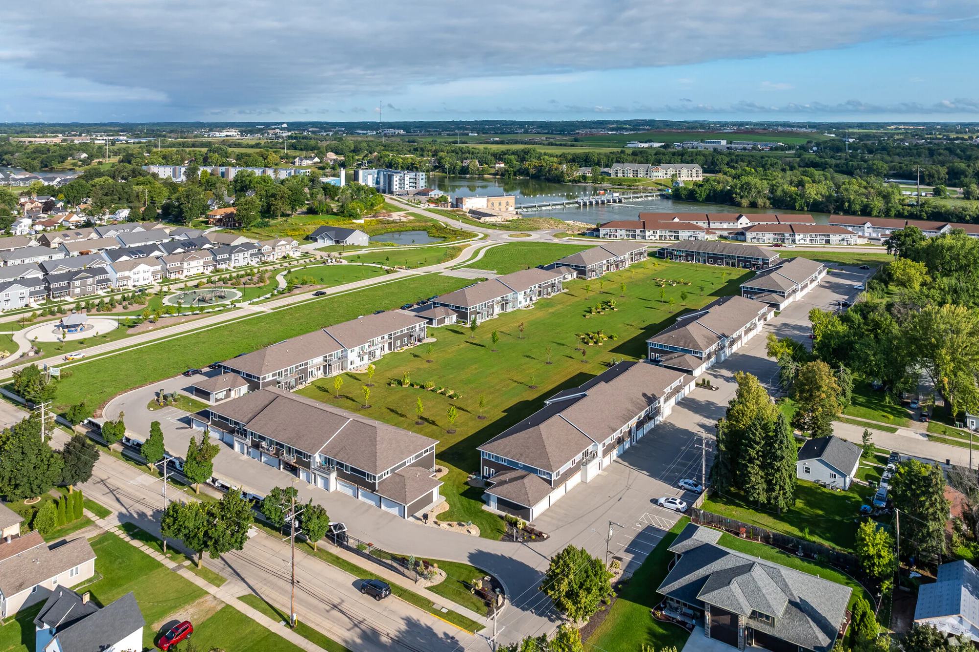 Aerial view of The Current Roots: eight two-story buildings with attached garages around a central green, Treaty Park at left, the Fox River and the Kimberly dam beyond